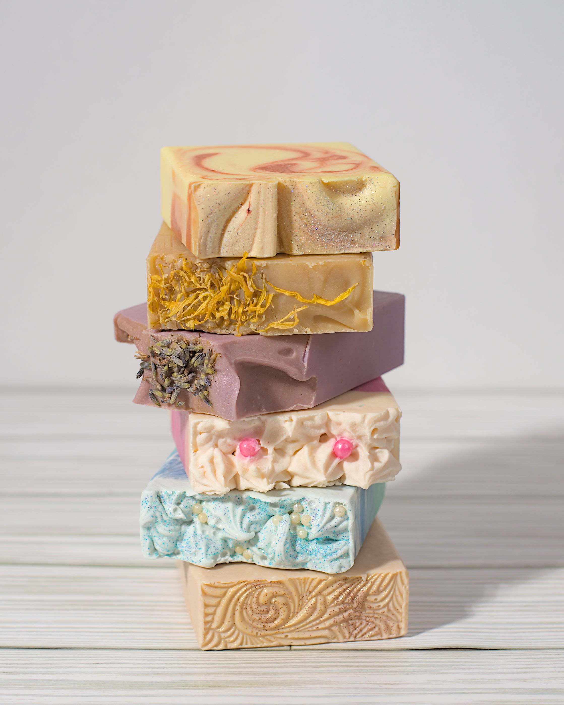 A vertical stack of artisan cold-process soaps focusing on the design details of the soap tops.